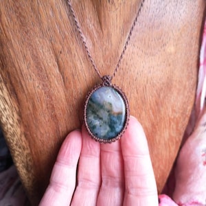 Puede incluir: Un collar de cordón marrón con un colgante de piedra de ágata verde, gris y blanca.