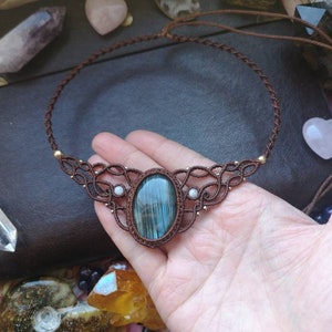 May include: A brown cord necklace with a large oval labradorite gemstone pendant and two smaller white gemstone accents. The necklace is knotted with a macrame design.