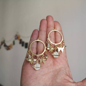 May include: Gold hoop earrings with dangling charms, including a butterfly, a star, and a globe with rhinestones.