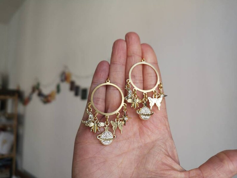 May include: Gold hoop earrings with dangling charms, including a butterfly, a star, and a globe with rhinestones.