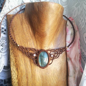 May include: A brown macrame necklace with a large oval-shaped labradorite gemstone pendant. The necklace is on a wooden mannequin.