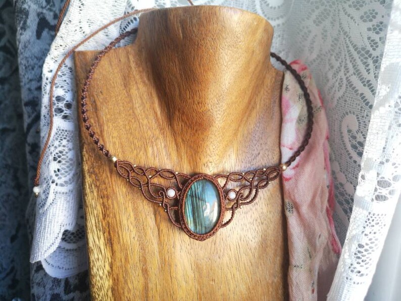 May include: A brown macrame necklace with a large oval-shaped labradorite gemstone pendant. The necklace is on a wooden mannequin.