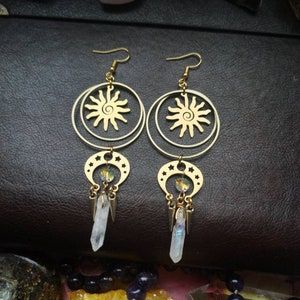 May include: Gold earrings with a sun and moon design. The earrings feature a circle with a sun design and a crescent moon with stars. The earrings are accented with clear crystals.