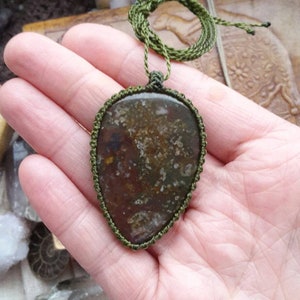 May include: A green cord necklace with a brown and green agate pendant. The pendant is wrapped in green cord and has a natural, organic look.