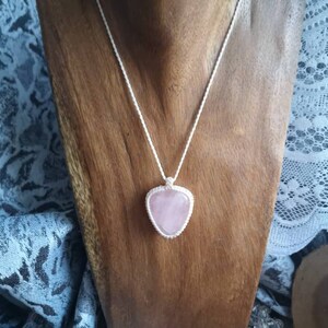 May include: A silver chain necklace with a pink heart-shaped pendant made of rose quartz.