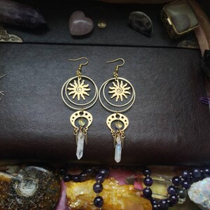 May include: Gold earrings with a sun and moon design. The earrings have a dangling crystal charm.