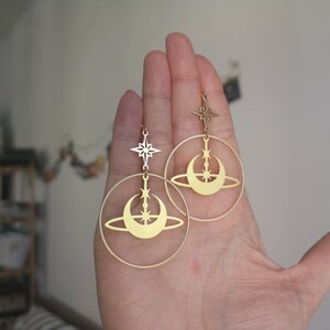 May include: Gold hoop earrings featuring a crescent moon and star design. The earrings dangle from a small star charm.