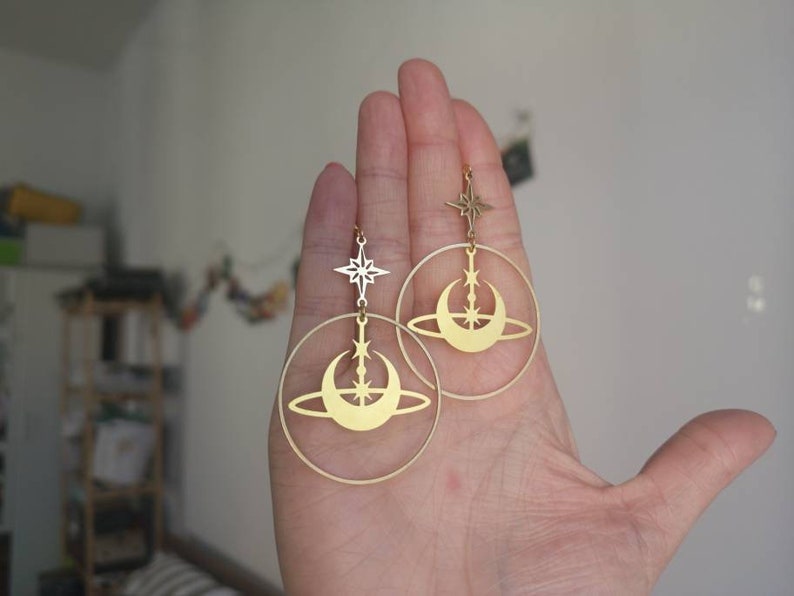 May include: Gold hoop earrings featuring a crescent moon and star design. The earrings dangle from a small star charm.