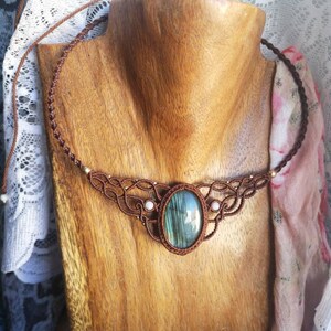 May include: A brown cord necklace with a large oval-shaped labradorite gemstone pendant. The necklace is accented with small white beads and has a knotted design.
