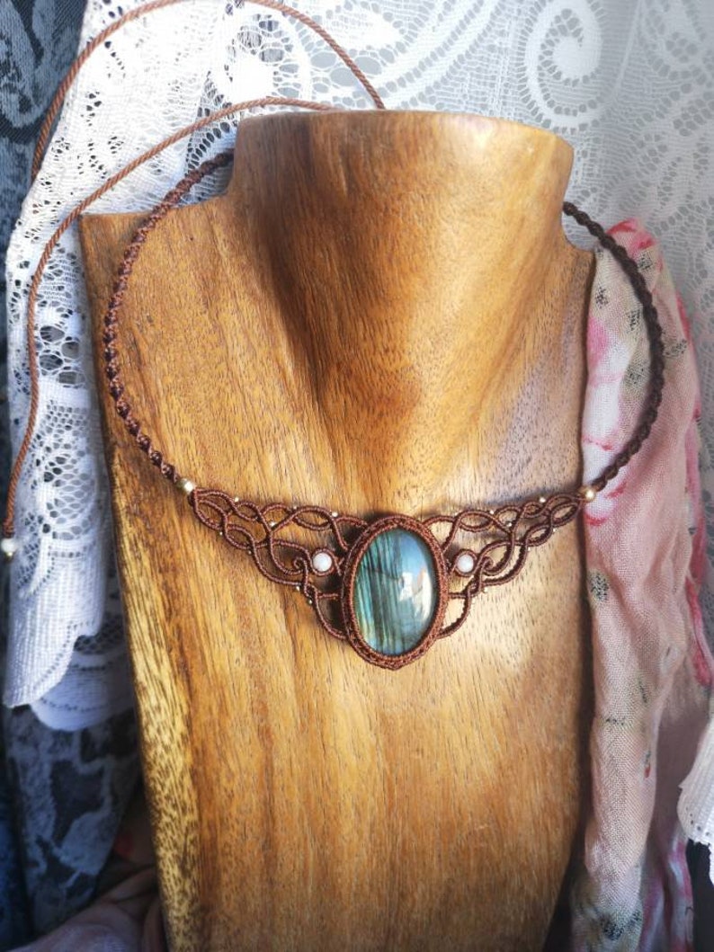 May include: A brown cord necklace with a large oval-shaped labradorite gemstone pendant. The necklace is accented with small white beads and has a knotted design.