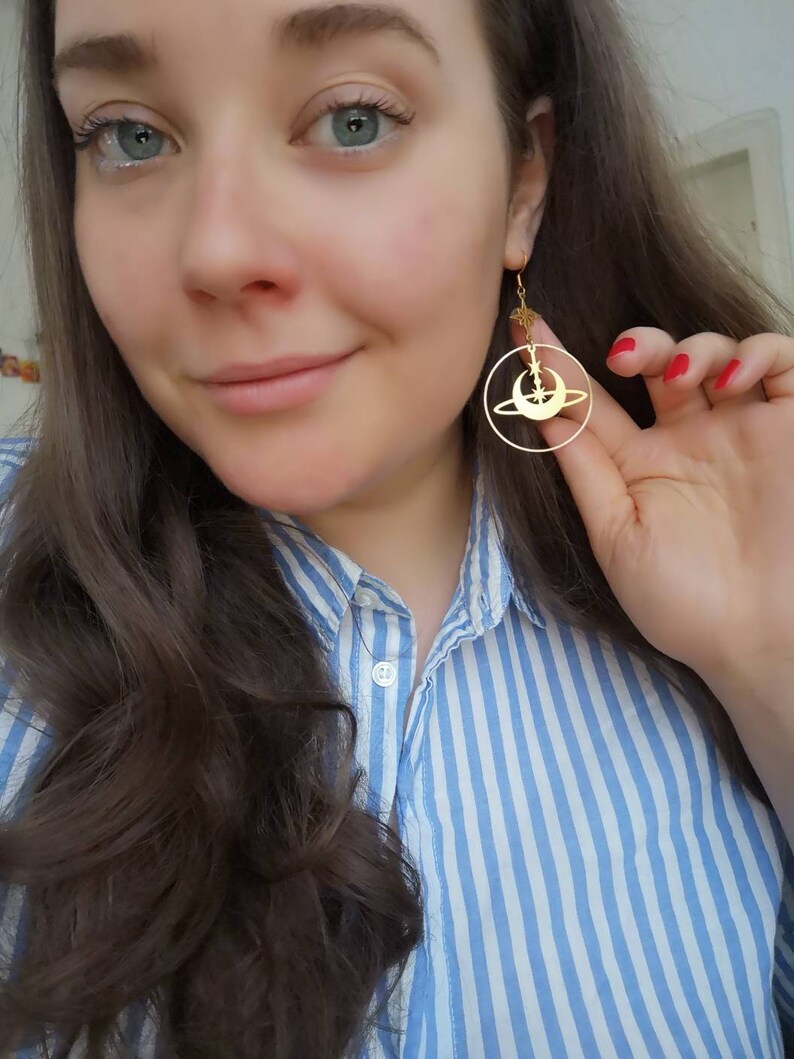 May include: Gold hoop earrings with a crescent moon, star, and ring design.