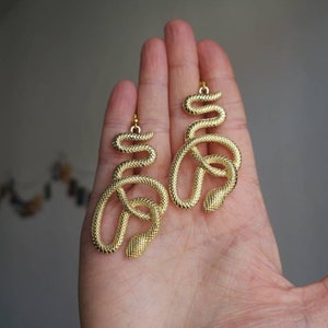 May include: A pair of gold snake-shaped earrings. The earrings are made of metal and have a textured surface.