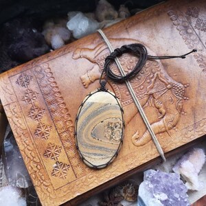 May include: A brown and white striped stone pendant on a brown leather cord. The pendant is hanging on a brown leather journal with an embossed elephant design.