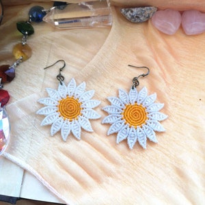 Op de afbeelding: Een paar witte madeliefjes oorbellen met gele centra. De oorbellen zijn gemaakt met macramé en hebben een eenvoudig, elegant ontwerp.