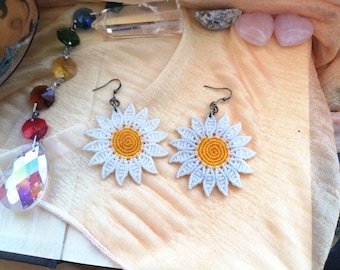 May include: A pair of white daisy earrings with yellow centers. The earrings are made with macrame and have a simple, elegant design.