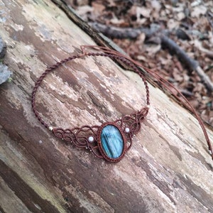 May include: A brown macrame necklace with a blue and green gemstone pendant and white pearl accents.