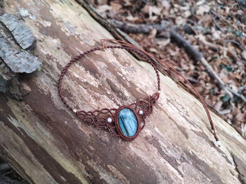May include: A brown macrame necklace with a blue and green gemstone pendant and white pearl accents.