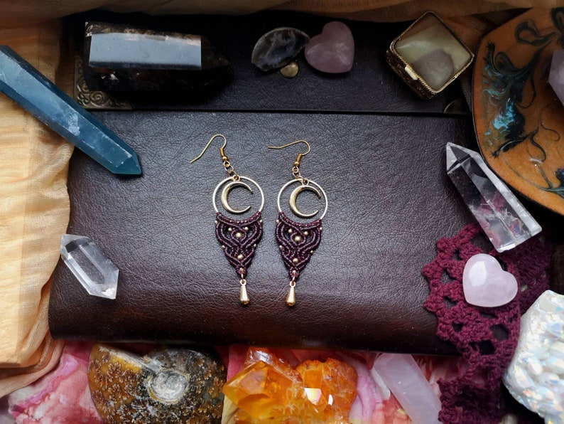 May include: A pair of maroon and gold earrings with a crescent moon charm and a macrame design.