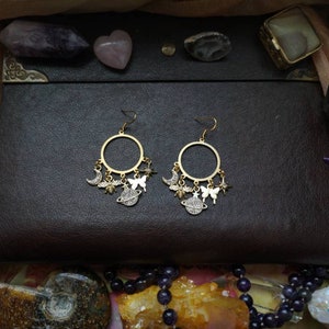 May include: Gold hoop earrings with dangling charms, including a crescent moon, a butterfly, a planet, and a star. The charms are silver with clear rhinestones.