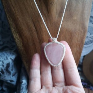 May include: A pink heart-shaped crystal pendant on a white macrame cord necklace.
