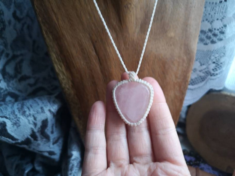 May include: A pink heart-shaped crystal pendant on a white macrame cord necklace.