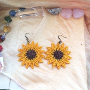 May include: A pair of sunflower earrings made with macrame. The earrings are yellow with brown centres and have a simple hook closure.