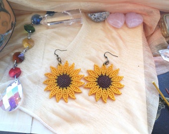 May include: A pair of sunflower earrings made with macrame. The earrings are yellow with brown centers and have a simple hook closure.