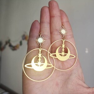 May include: Gold hoop earrings with a crescent moon and star design. The earrings feature a dangling star charm.