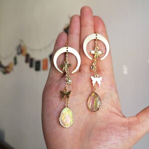 Puede incluir: Pendientes de media luna dorados con colgantes, incluyendo mariposas, lib&eacute;lulas y piedras iridiscentes en forma de l&aacute;grima.