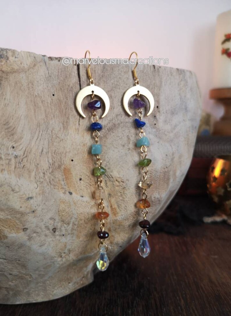 May include: Gold crescent moon earrings with a dangling chain of colorful gemstones, including amethyst, lapis lazuli, aventurine, peridot, citrine, carnelian, and garnet, ending with a clear crystal drop.