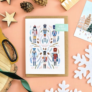 May include: A festive Christmas card featuring nutcracker illustrations, complemented by wooden stars, pine cones, and a snowflake. The card includes the text "Christmas Wishes" and a label that says "Amber Davenport".
