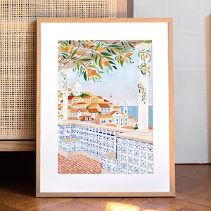 Op de afbeelding: Een ingelijste illustratie van een stadsgezicht met een betegeld balkon met uitzicht op de zee. De stad is geschilderd in warme kleuren met een blauw en wit betegeld balkon op de voorgrond. De illustratie is ingelijst in een licht houten lijst.