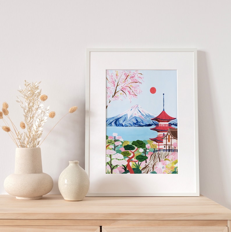 May include: A framed illustration of Mount Fuji with a red pagoda in the foreground. The mountain is surrounded by a blue lake and a lush green forest with pink cherry blossoms. A red sun is visible in the sky.