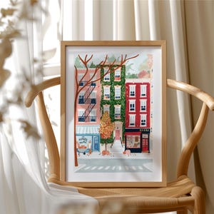 May include: A framed art print showing a street scene with vibrant buildings. The buildings are pink, green, and red, with a flower market and a bookstore. The print is displayed on a wooden chair.