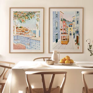 May include: Two framed art prints depicting scenes of Portugal. One shows a coastal view with orange trees and blue tilework. The other features a yellow tram on a cobblestone street lined with colorful buildings.
