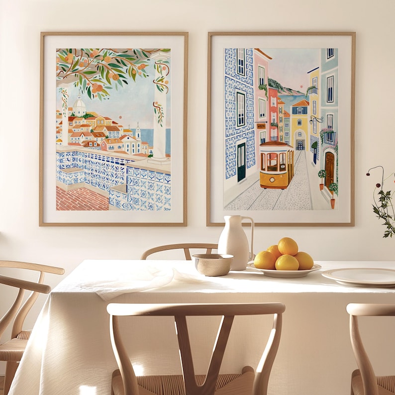May include: Two framed art prints depicting scenes of Portugal. One shows a coastal view with orange trees and blue tilework. The other features a yellow tram on a cobblestone street lined with colorful buildings.