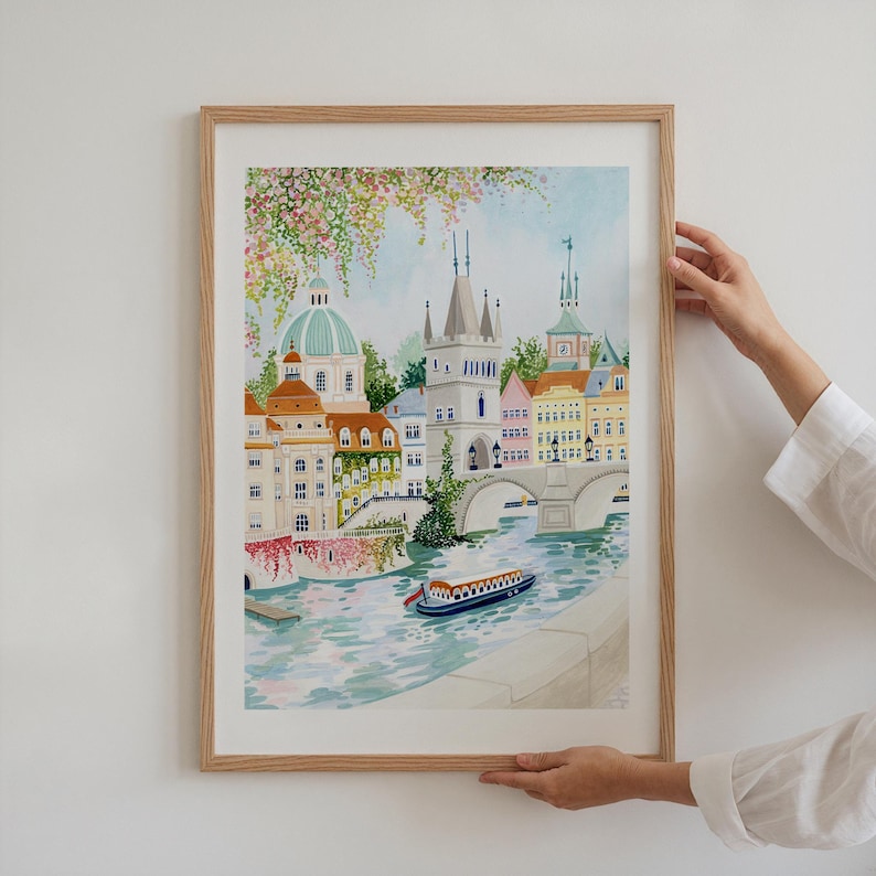 May include: A watercolor painting of a cityscape with a bridge over a river. The buildings are colorful and have pointed roofs. There are trees and flowers in the foreground. A small boat is in the river.