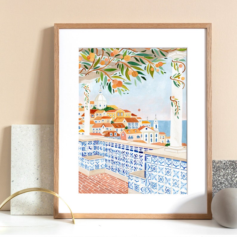 Op de afbeelding: Een aquarel schilderij van een stadsgezicht met een betegeld balkon met uitzicht op de zee. De sc&egrave;ne toont een wit gebouw met een koepel, kleurrijke huizen en een fel oranje zon die ondergaat boven het water. Het balkon is versierd met blauwe en witte tegels.
