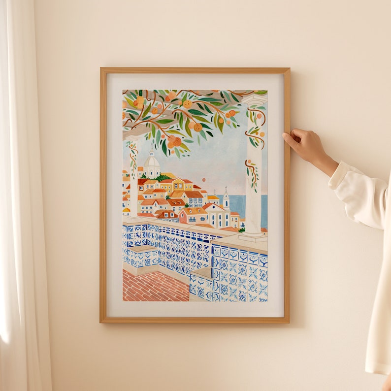 Op de afbeelding: Een aquarel schilderij van een stadsgezicht met een betegeld balkon met uitzicht op de zee. De stad is geschilderd in warme kleuren, met een wit gebouw in het midden. Het balkon is versierd met blauwe en witte tegels. Het schilderij is ingelijst in een licht houten lijst.