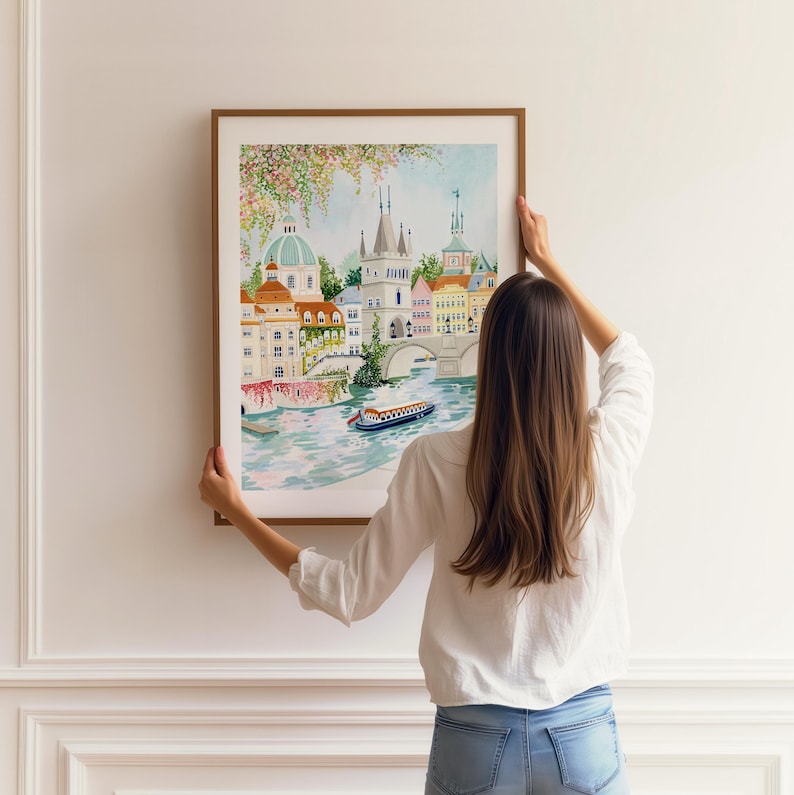 May include: A watercolor painting of a cityscape with a bridge and a boat. The buildings are painted in shades of pink, yellow, and blue. The bridge is a white arch bridge with a green railing. The boat is a small, white boat with a blue roof.