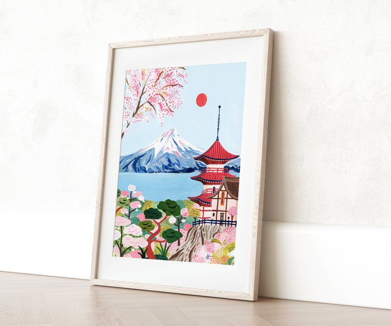 May include: A framed illustration of Mount Fuji with a red pagoda in the foreground. The mountain is snow-capped and the pagoda has a red roof and white walls. There are pink cherry blossoms in the trees and a red sun in the sky.