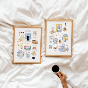 May include: Two framed art prints with wooden frames, featuring colorful illustrations of Lisbon and Portuguese culture. The left print says "Lisboa" and includes images of food, drinks, and landmarks. The right print says "Bom Dia" and includes images of food, a guitar, and a dress.
