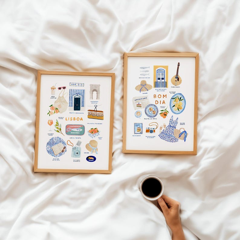 May include: Two framed art prints with wooden frames, featuring colorful illustrations of Lisbon and Portuguese culture. The left print says "Lisboa" and includes images of food, drinks, and landmarks. The right print says "Bom Dia" and includes images of food, a guitar, and a dress.