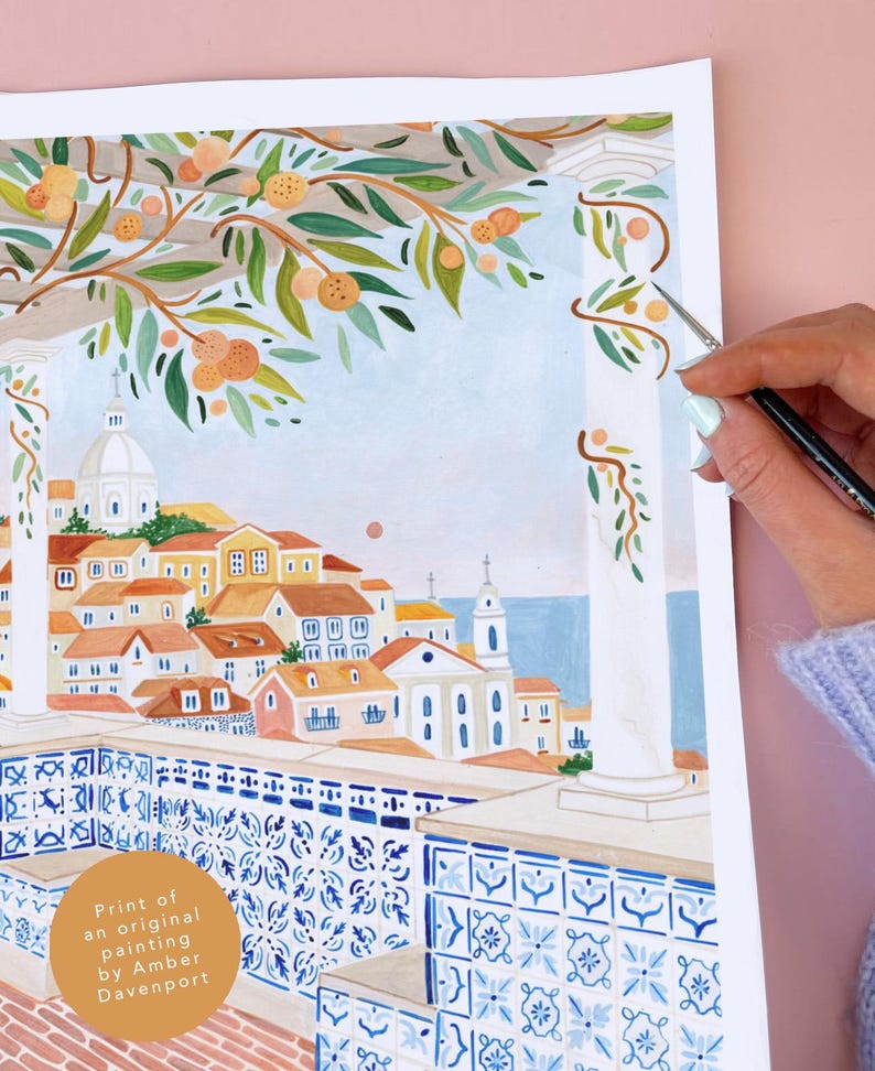 May include: Watercolor print of a coastal town scene. The artwork features buildings with orange roofs, a blue sea, and a decorative balcony with blue and white tiles. Branches with oranges and green leaves frame the top.