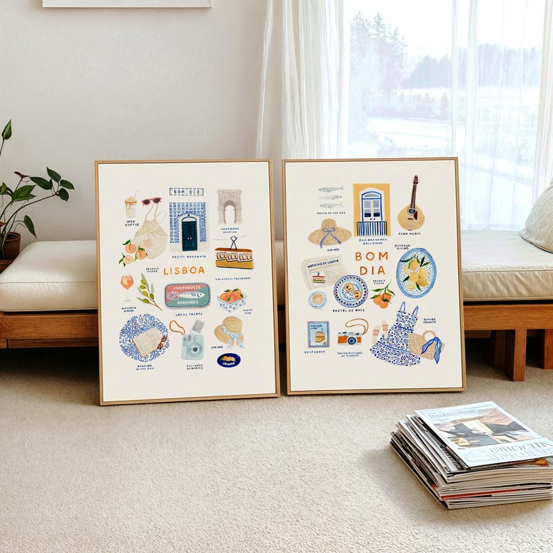 May include: Two framed art prints with illustrations of Lisbon and "Bom Dia" scenes. The Lisbon print features a blue door, oranges, and a camera. The "Bom Dia" print includes a guitar, a dress, and a plate of food. Both prints have a light wood frame.
