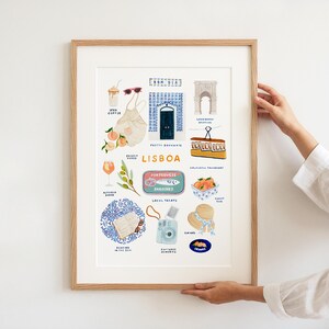 May include: A framed art print featuring illustrations of Lisbon, Portugal. The print includes images of a tram, sardines, oranges, a camera, and a blue door. The text "LISBOA" is prominently displayed.