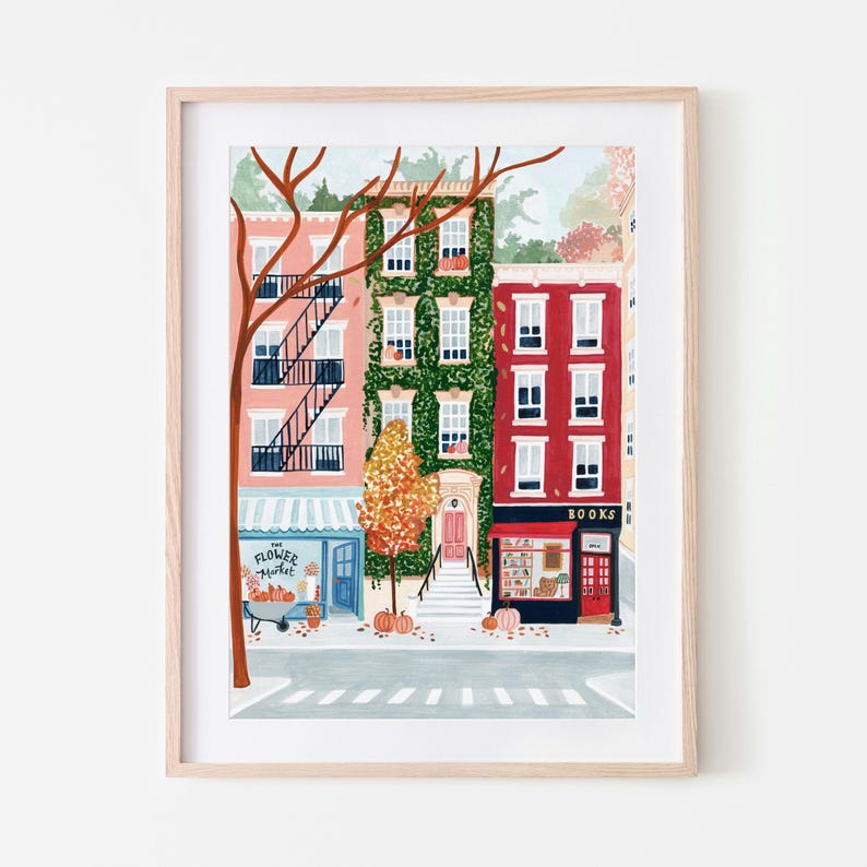 May include: An art print depicting a city street scene with three buildings in autumn. The buildings are pink, green, and red, with a flower market and a bookstore. Pumpkins and fall foliage are scattered throughout.