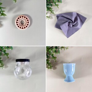 K&ouml;nnte beinhalten: Eine Sammlung von Haushaltsgegenst&auml;nden: ein Holzuntersetzer mit geometrischem Design, ein lavendelfarbenes Mikrofasertuch, ein kleines Glas mit schwarzem Deckel und ein hellblauer Eierbecher. Auf neutralem Hintergrund angeordnet.