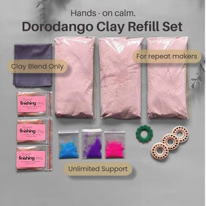 May include: A Dorodango Clay Refill Set featuring three large bags of light pink clay powder, three small bags of finishing clay, three small bags of blue, purple, and pink pigment, a purple cloth, one green ring, and three circular wooden discs.