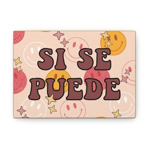 May include: A pink and yellow canvas print with a repeating pattern of smiley faces and stars. The print features the text "Si Se Puede" in brown letters.